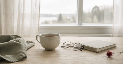 Kalt gewordene Tasse Tee neben Lesebrille und Buch