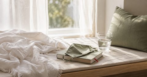 Fensterplatz mit Decke, Buch und Stoffmaske